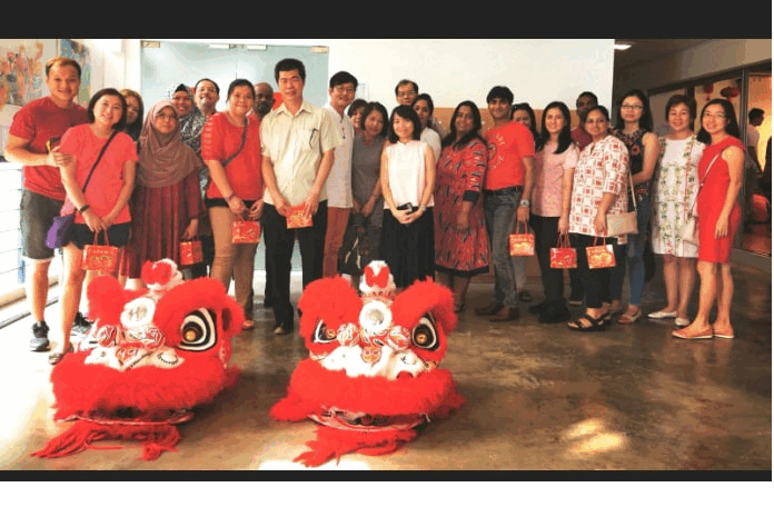 A group of people in red clothing pose behind two red Chinese lion dance costumes indoors.
